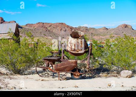 Nelson, Nevada - 15 aprile 2024: Miscelatore a mano arrugginito vintage e carriola si trovano all'aperto nella città fantasma di Nelson. Foto Stock