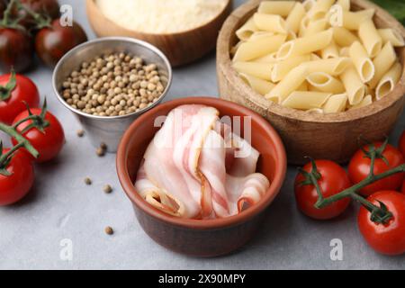 Pasta cruda, pancetta e ingredienti freschi su un tavolo grigio chiaro Foto Stock