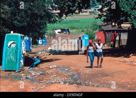 Kliptown, Soweto Johannesburg. Due giovani donne/ragazze camminavano su una strada non asfaltata fuori dai bagni. baracche nella povertà di fondo. Adolescenti. Foto Stock