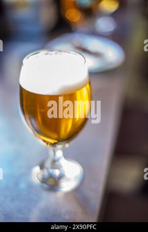 Un bicchiere di tulipano pieno di birra frizzante si trova in un bar in Spagna, catturato con un obiettivo vintage ad ampia apertura. Foto Stock