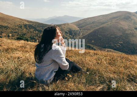 Donna siede con la schiena nel campo di montagna e ammira il tramonto sulle montagne. Foto Stock