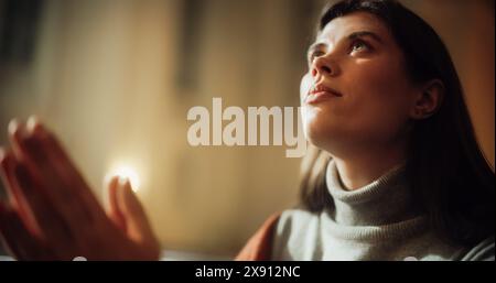 La donna cristiana siede piamente nella Chiesa, pregando, cerca la guida e il conforto dalla fede religiosa e dalla fede spirituale in Dio. Telecamera che mostra le sue mani di preghiera e il suo volto speranzoso Foto Stock