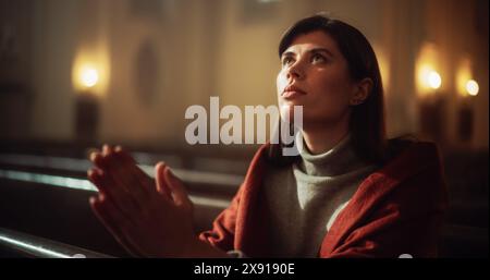 Una devota donna cristiana siede piamente in una Chiesa, piegando le mani per pregare, cerca di guidare la sua fede religiosa e la sua spiritualità. Spirito del cristianesimo e fede nella bontà di Dio Foto Stock