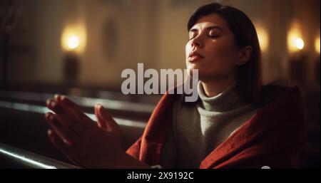 La giovane donna cristiana siede con pietà nella Chiesa maestosa, con le mani piegate cerca la guida della fede e della spiritualità mentre prega. Fede religiosa nel potere e nell'amore di Dio. Ripresa cinematografica Foto Stock