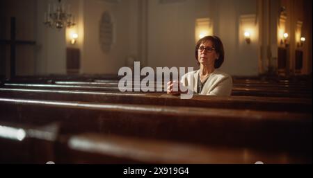 Ritratto di una Pia donna anziana che prega mentre siede nella Vecchia Chiesa. Parrocchiano che sente connessione con la divinità. Speranza, fede nella salvezza attraverso la bontà, la gentilezza. Contemplazione nella Cattedrale Foto Stock