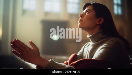 Una devota donna cristiana siede piamente in una Chiesa, piegando le mani per pregare, cerca di guidare la sua fede religiosa e la sua spiritualità. Spirito del cristianesimo e fede nella bontà di Dio Foto Stock