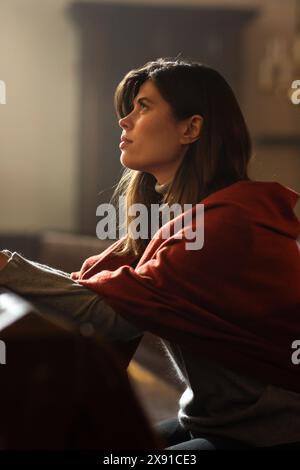 Una devota donna cristiana siede piamente in una Chiesa, piegando le mani per pregare, cerca di guidare la sua fede religiosa e la sua spiritualità. Spirito del cristianesimo e fede nella bontà di Dio Foto Stock