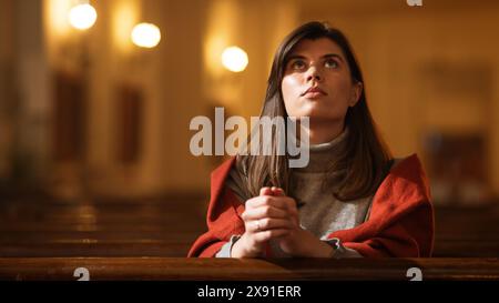 Una devota donna cristiana siede piamente in una Chiesa, piegando le mani per pregare, cerca di guidare la sua fede religiosa e la sua spiritualità. Spirito del cristianesimo e fede nella bontà di Dio Foto Stock