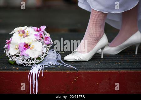 Eleganti scarpe bianche e calze rosa accanto a un bouquet di fiori bianchi e rosa su un pavimento in legno Foto Stock