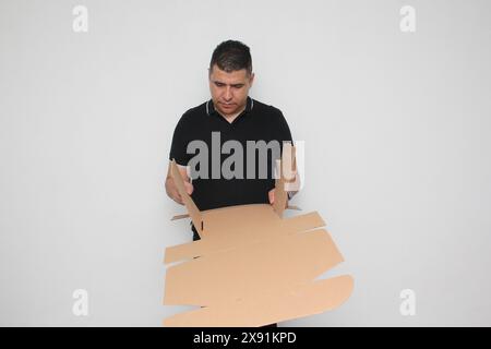 L'uomo adulto latino assembla una scatola di cartone seguendo le istruzioni per raggiungerla Foto Stock