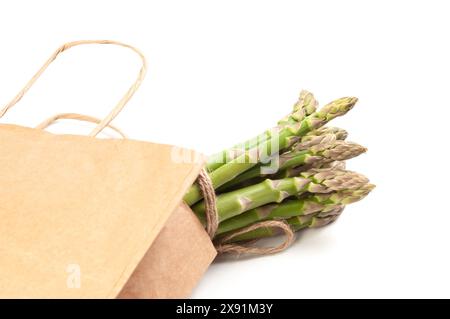 Un fascio di gambi di asparagi verdi freschi è disposto in modo ordinato in un sacchetto di carta marrone, ben visibile su sfondo bianco. Foto Stock