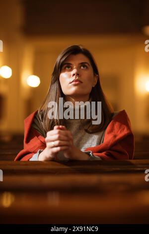 Una devota donna cristiana siede piamente in una Chiesa, piegando le mani per pregare, cerca di guidare la sua fede religiosa e la sua spiritualità. Spirito del cristianesimo e fede nella bontà di Dio Foto Stock