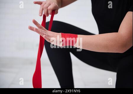 Primo piano forte pugile donna che prepara bende da pugilato, avvolgendosi il polso e le mani con un nastro rosso, prima di indossare guanti da boxe, si riprende Foto Stock