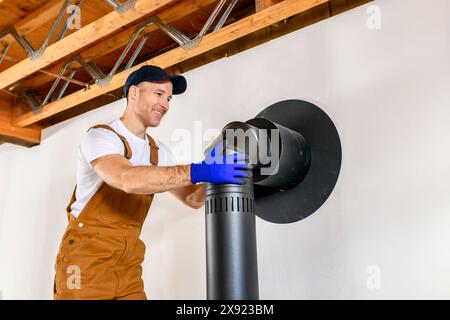 lavoratore maschile che prepara un'installazione di camini per una moderna stufa riscaldante a risparmio energetico. Foto Stock