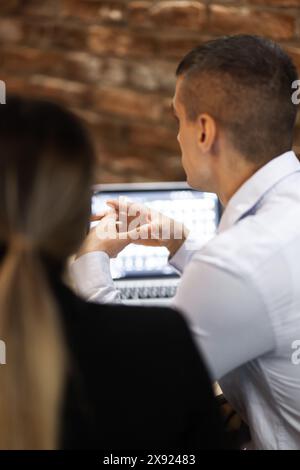 Due professionisti impegnati in una riunione di lavoro in un ambiente elegante con schermo visibile per computer. L'attenzione è rivolta all'altoparlante maschile. Foto Stock