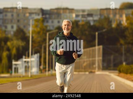 Felice e felice sportivo maturo in pensione che fa sport e corre allo stadio al mattino. Foto Stock