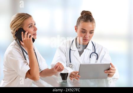 Due donne, una sul suo portatile, l'altra con il suo tablet personale sanitario in un ospedale durante una posa di rilassamento. 016644 027 Foto Stock