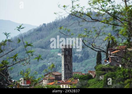 Il campanile della chiesa nel villaggio rurale di Benabbio vicino a bagni di Lucca in Toscana, Italia, in una giornata nuvolosa con alberi e vedute lontane. Foto Stock