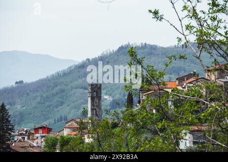 Il campanile della chiesa nel villaggio rurale di Benabbio vicino a bagni di Lucca in Toscana, Italia, in una giornata nuvolosa con alberi e vedute lontane. Foto Stock