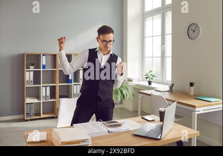 Contabile maschile che ottiene soddisfazione dal suo lavoro in ufficio e alza il pugno Foto Stock