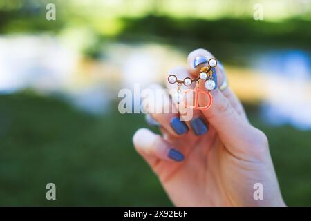 Una giovane donna mostra un orecchino d'oro e di perle nel palmo della mano in un ambiente naturale all'aperto, con le unghie dipinte di blu Foto Stock