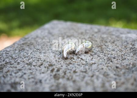 Composizione di un paio di orecchini in argento su una grande pietra di granito grezza. Gli orecchini sono a forma di goccia Foto Stock