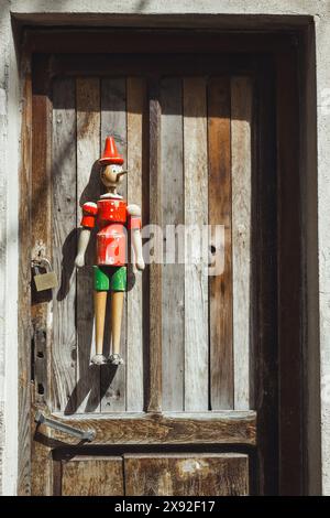 Un piccolo burattino giocattolo Pinocchio nella storica città italiana di Collodi, sede del Parco Pinocchio e di una splendida città vecchia. Appeso su una porta di legno. Foto Stock
