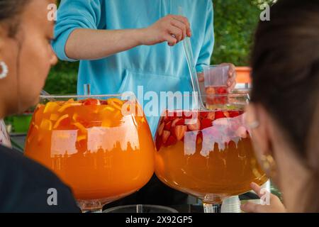 fila di grandi ciotole di vetro piene di varie bevande colorate e diversi tipi di frutta. bevande punch con ananas, fragole e latte Foto Stock