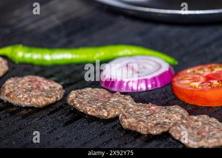 Lo chef sta cucinando polpette sulla griglia. Tagliate le polpette a pezzetti pronti per la cottura alla griglia. Lo chef sta girando le polpette. Foto Stock