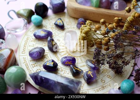 Rune scandinave fatte di ametista ed erbe secche su sfondo rosa con un tabellone con simboli dei segni zodiacali. Previsioni, stregoneria, spiritu Foto Stock