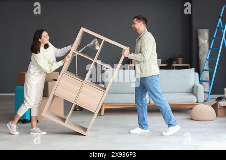 Felice giovane coppia che trasporta un ripiano in camera il giorno del trasloco Foto Stock