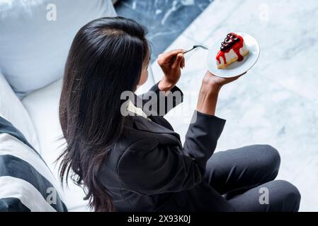 Una donna felice mangia una torta un delizioso dolce nel caffè al cioccolato. Donna asiatica che tiene la forchetta mangiando una torta dolce fantasia, un piatto di zucchero gustoso nel bar. WOM Foto Stock