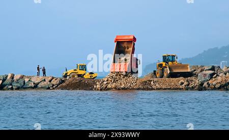 Costruzione di Breakwater sulla costa marittima. Il dumper scarica pietre. Lavorare venicole intorno. Batumi, Georgia. Foto di alta qualità Foto Stock