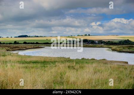 Cuckmere Haven, Regno Unito - 10 settembre 2022: Veduta di Cuckmere Haven che mostra l'acqua in primo piano e i campi e gli edifici sullo sfondo Foto Stock