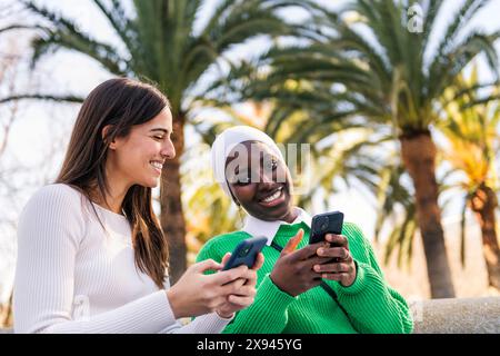 amiche che usano il cellulare seduto al parco Foto Stock