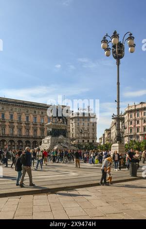 Persone che camminano in Piazza del Duomo, sotto la statua del re Vittorio Emanuele II (1896) in un giorno d'auto di sole, Milano, Lombardia, Italia Foto Stock