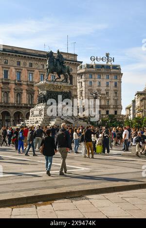 Persone che camminano in Piazza del Duomo, sotto la statua del re Vittorio Emanuele II (1896) in un giorno d'auto di sole, Milano, Lombardia, Italia Foto Stock