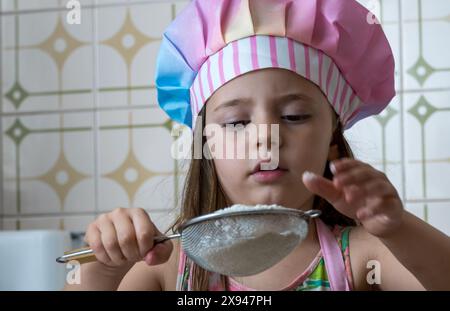 una ragazza vestita da cuoca che si gode un pomeriggio di cucina con sua madre Foto Stock