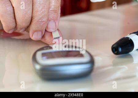 Primo piano della mano introduzione della striscia reattiva sul monitor dello zucchero per controllare i livelli di glucosio nel sangue Foto Stock