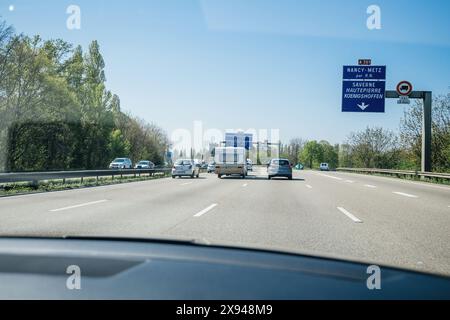 Alsazia, Francia - 19 aprile 2019: Una vista dall'interno di un'auto su un'autostrada francese, con diversi veicoli, segnali stradali e vegetazione, in direzione Metz in una giornata limpida Foto Stock