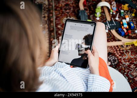 Parigi, Francia - 11 giugno 2023: Una donna è seduta e sta leggendo su un iPad l'Apple Vision Pro, concentrandosi sulle caratteristiche dettagliate delle cuffie, circondate da giocattoli per bambini sul pavimento Foto Stock