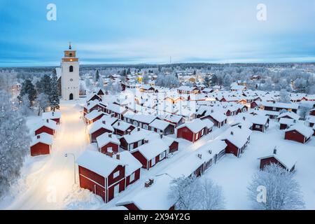 Vista aerea invernale della vecchia Gammelstad illuminata, coperta di neve con cottage rossi intorno alla chiesa, Gammelstad Church Town, UNESCO, Svezia Foto Stock