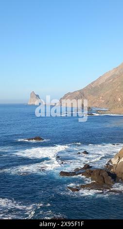 Splendido paesaggio costiero con aspre scogliere, onde oceaniche blu e lontane affioramenti rocciosi sotto un cielo azzurro Foto Stock