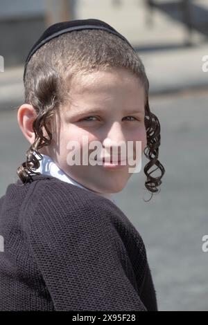 Un ritratto in posa di un ragazzo ebraico chassidico con lungo peyus riccio. A una festa del LAG B'Omer a Brooklyn, New York. Foto Stock