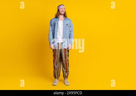 Foto a tutto corpo di un giovane uomo hippie che posa un modello a vuoto indossa un abito di tendenza in denim isolato su sfondo giallo Foto Stock