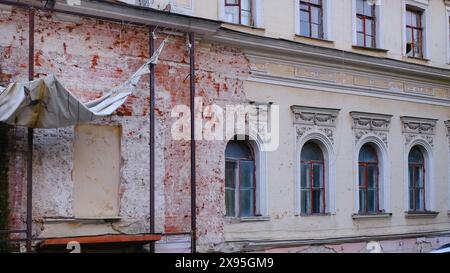 Frammento di facciata con finestre in rovina e sbriciolati intrecci in stucco di un vecchio edificio abbandonato. Antico edificio distrutto pronto per essere demolito. Foto Stock