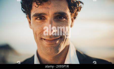 Primo piano Ritratto di un giovane adulto felice maschio con capelli ricci e occhi marroni in posa per la fotocamera. Bell'uomo caucasico multietnico in una tuta sorridente. Modifica colore caldo. Foto Stock
