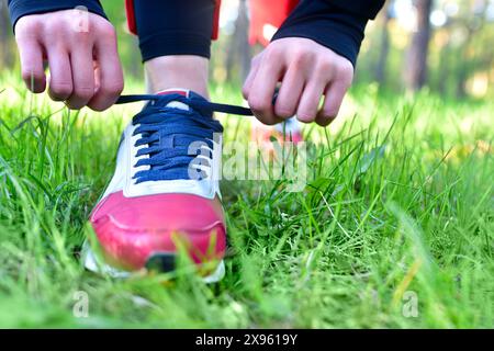 Una donna stringe i lacci sulle sue sneaker atletiche in un parco mentre fa jogging Foto Stock