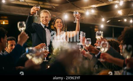 Gli sposi e gli sposi festeggiano il matrimonio a una festa di ricevimento serale. Gli sposi propongono un brindisi al matrimonio felice, in piedi a un tavolo da pranzo con i migliori amici multietnici e diversificati. Foto Stock