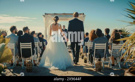 Splendida sposa in abito da sposa bianco e bel guardaroba in un tradizionale abito nero che scende lungo la navata in un luogo per cerimonie all'aperto vicino al mare con amici felici multietnici e diversi. Foto Stock